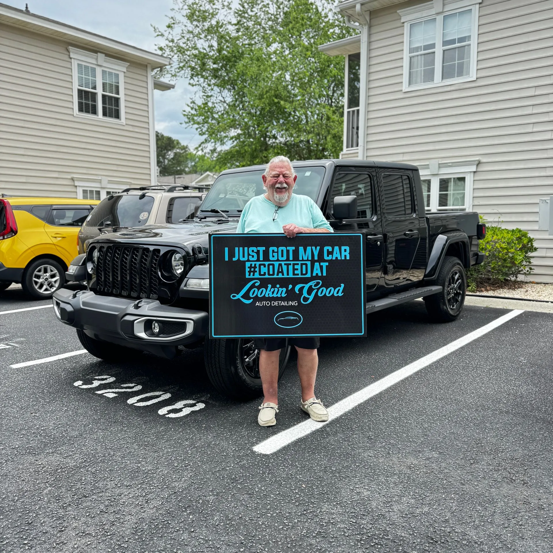 Client holding a #COATED sign beside a coated Jeep Gladiator