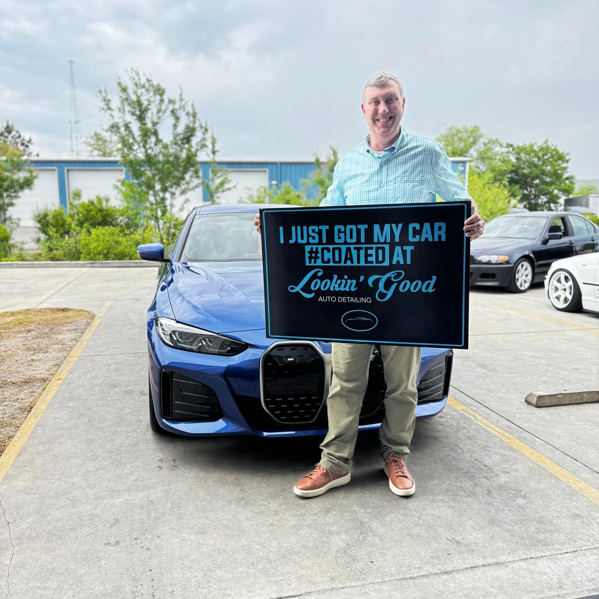 Client holding a #COATED sign beside a coated blue BMW i4