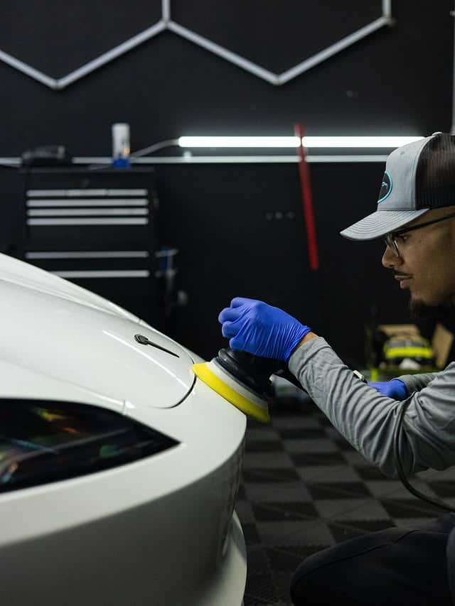 Machine polishing the fender of a white Tesla before coating